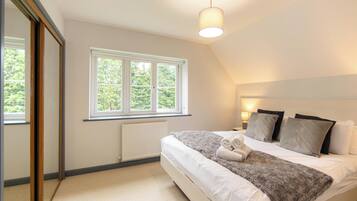 A bedroom with a large window, a bed with pillows and a blanket, a bedside lamp, and a radiator.