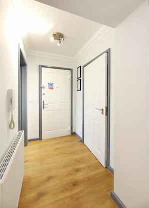 A hallway with wooden flooring, white walls, and a white door at the end.