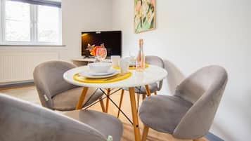A dining area with a round table, two grey chairs, a television, and a painting on the wall.