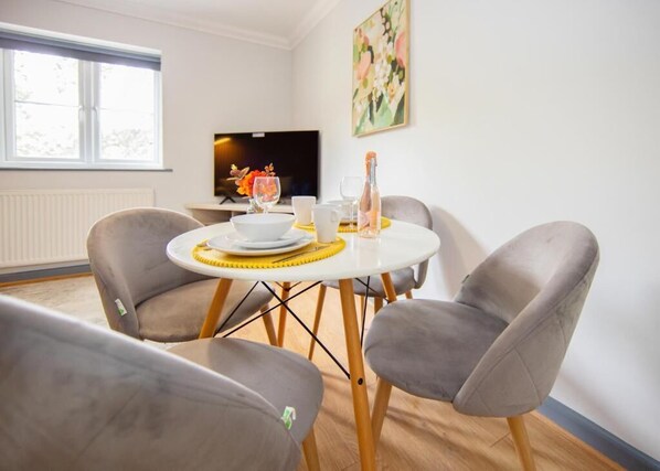 A dining area with a round table, two grey chairs, a television, and a painting on the wall.