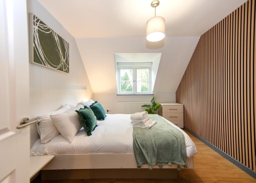 Un dormitorio con cama, ventana, radiador y pared con líneas verticales.