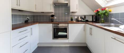 A modern kitchen with white cabinets, a built-in oven, a coffee machine, and a skylight.