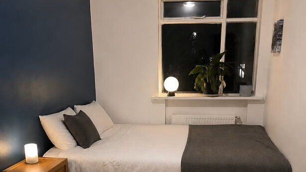 Un dormitorio con cama, mesita de noche, lámpara y ventana con vistas al exterior.