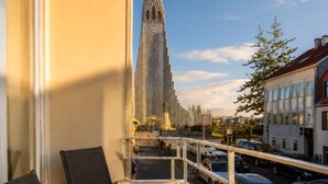Un balcón con vistas a la aguja alta de una iglesia, una mesa con sillas y una planta en maceta.