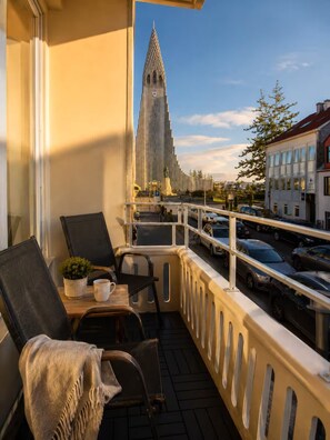 Ein Balkon mit Blick auf ein hohes Kirchturmdach, einem Tisch mit Stühlen und einem Blumentopf.