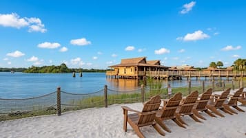 Un resort frente a la playa con cabañas de madera, una playa de arena y un lago tranquilo.