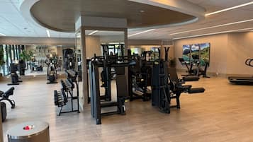 A gym with various exercise equipment, a wooden floor, and a large mirror.