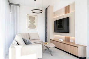 Ein modernes Wohnzimmer mit einer Couch, einem Couchtisch, einem flachbildfernseher an der Wand und einer minimalistischen Einrichtung.
