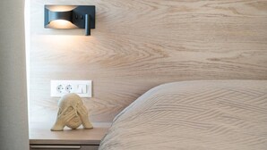 A neatly made bed with a textured blanket, a wall-mounted light fixture, and a power outlet on a wooden bedside table. - Sofia`s Estates : Villa Savvas (Adults Only) (Lagoudi Zia)