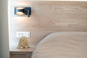 A neatly made bed with a textured blanket, a wall-mounted light fixture, and a power outlet on a wooden bedside table. - Sofia`s Estates : Villa Savvas (Adults Only) (Lagoudi Zia)