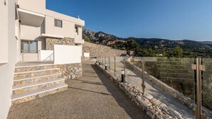 A modern building with a stone staircase leading to a white entrance, surrounded by a rocky landscape and mountains in the background. - Sofia`s Estates : Villa Savvas (Adults Only) (Lagoudi Zia)