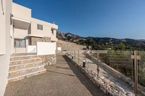 A modern building with a stone staircase leading to a white entrance, surrounded by a rocky landscape and mountains in the background. - Sofia`s Estates : Villa Savvas (Adults Only) (Lagoudi Zia)