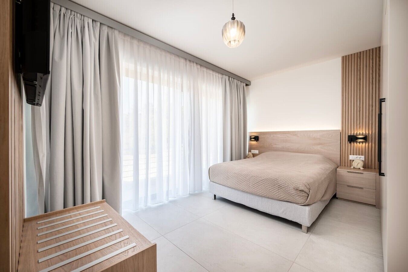 Een moderne slaapkamer met een groot bed, een nachtkastje, een hanglamp en een raam met gordijnen.