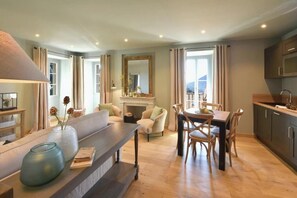 A modern living room with a fireplace, a dining area with wooden furniture, and a kitchen with dark cabinets. - Suite 3 at Maison Madamicella / heated pool (Corse-du-Sud)