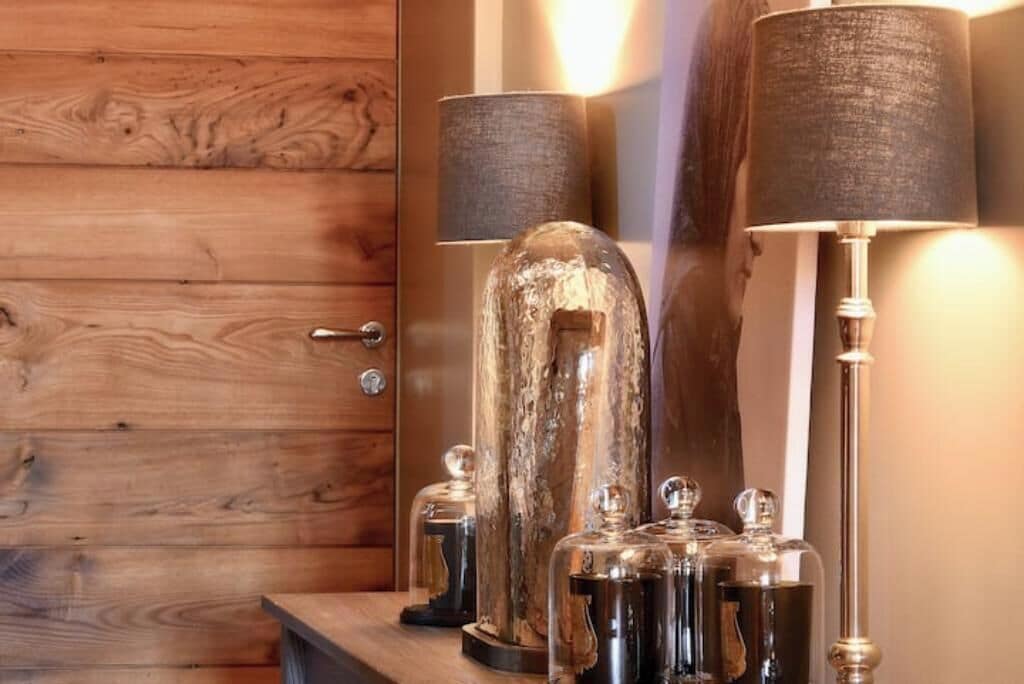 Une porte en bois avec une poignée en métal, un objet en verre à la surface texturée, et deux lampes dotées d’abat-jour cylindriques.