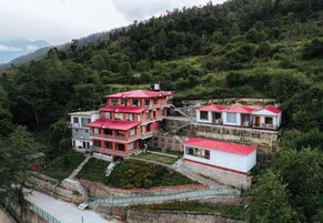 A multi-story hotel with red roofs, situated on a hillside with lush greenery in the background.