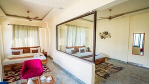 A hotel room with two beds, a large mirror, a seating area with a table, and a ceiling fan. - Aaryam Resort Auli (Joshimath)