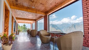 A covered outdoor seating area with wicker furniture and a view of mountains. - Aaryam Resort Auli (Joshimath)