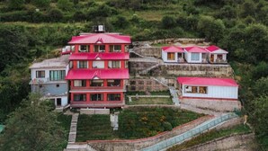 A multi-story building with a red roof, surrounded by lush greenery and terraced land. - Aaryam Resort Auli (Joshimath)