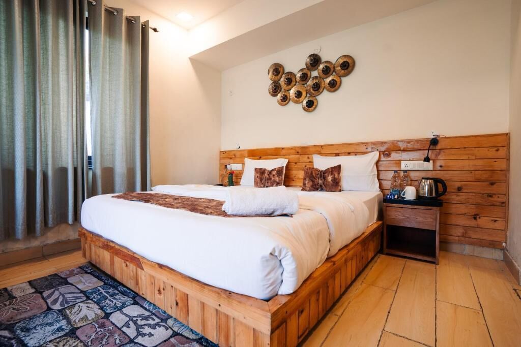 Un dormitorio con una cama de madera, un tapete estampado, una mesita de noche con una tetera y una lámpara de pared.