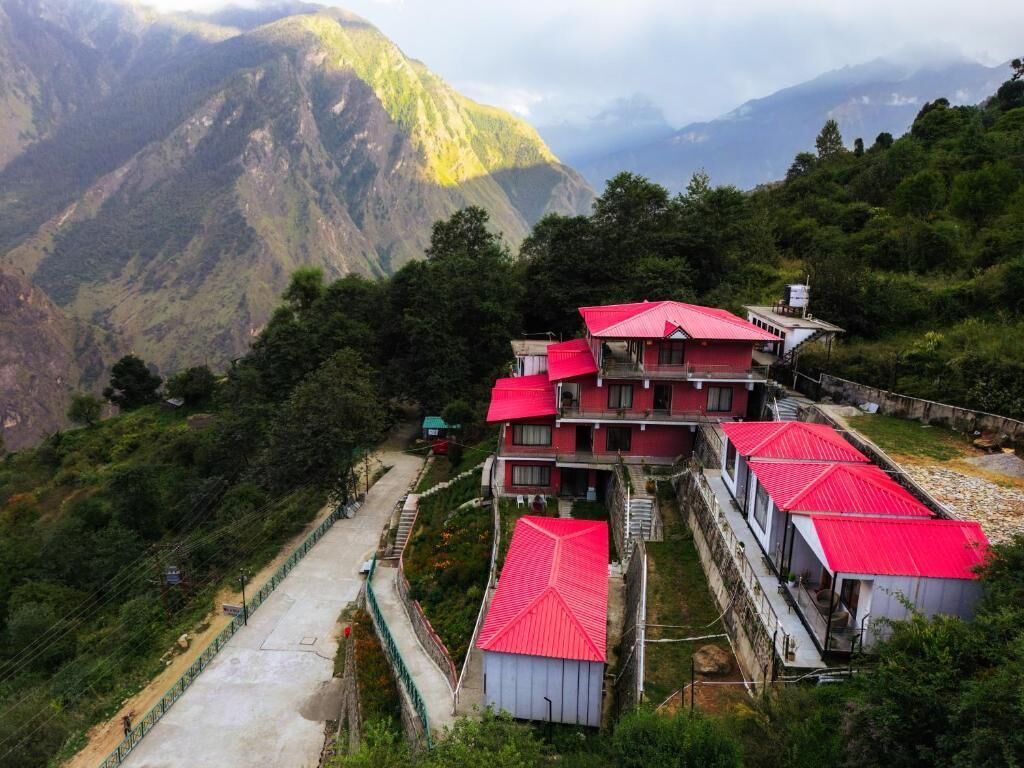 A cluster of buildings with red roofs, surrounded by lush greenery and mountains in the background.