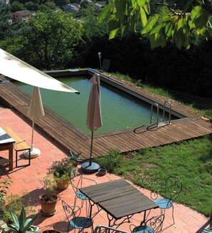 Eine Holzterrasse mit Pool, Gartenmöbeln und Topfpflanzen.