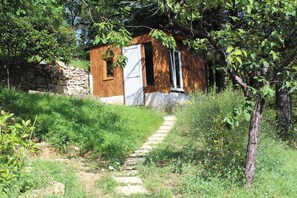 Eine rustikale Holzhütte mit einer Steinwand, einer Holztür und einem schmalen Steinweg, der dorthin führt.