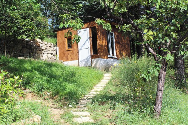 Una cabaña rústica de madera con un muro de piedra, una puerta de madera y un estrecho sendero de piedra que la conduce.