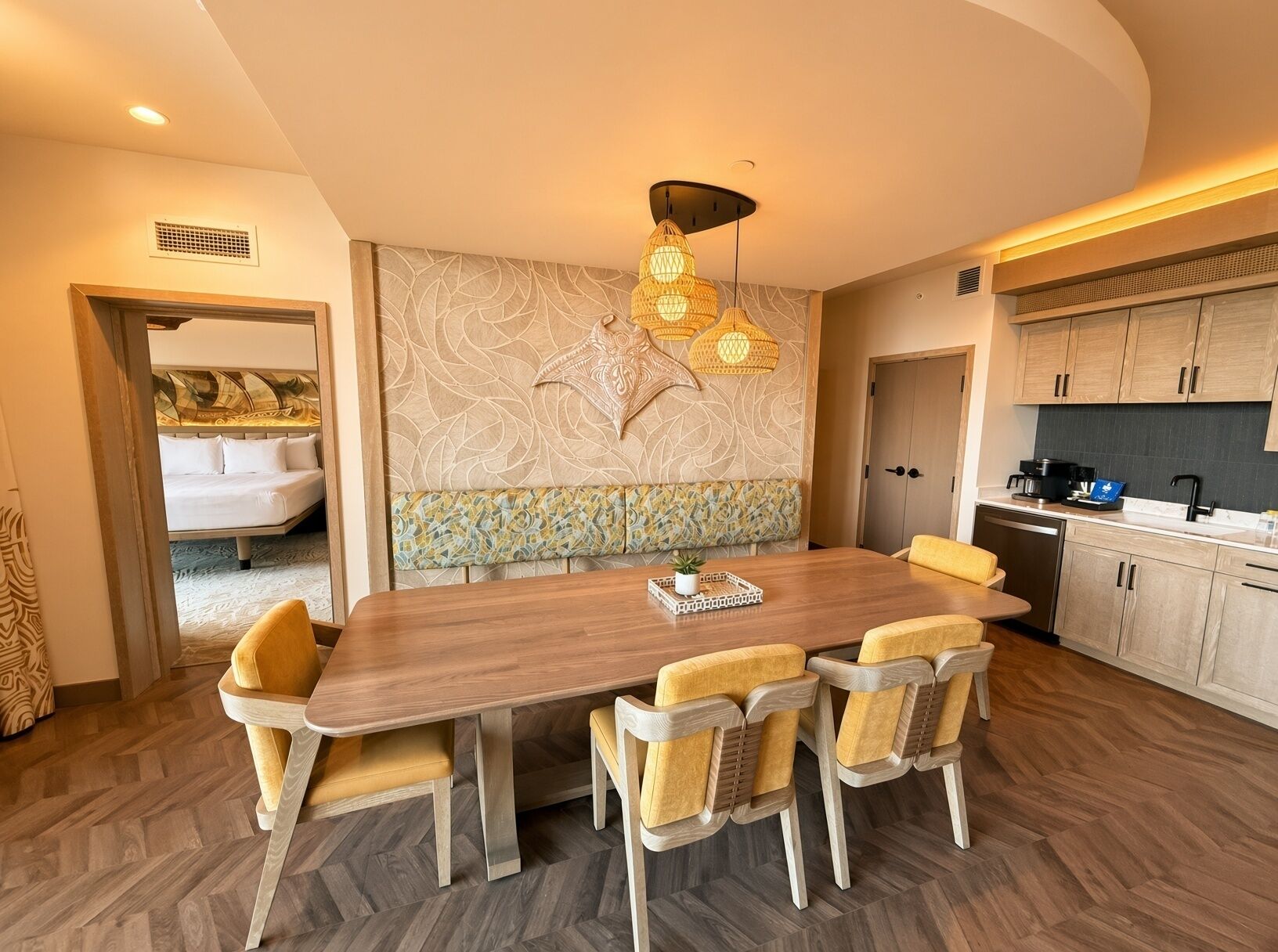 A modern kitchen with wooden cabinets, a dining table with chairs, and a decorative wall with a leaf pattern.