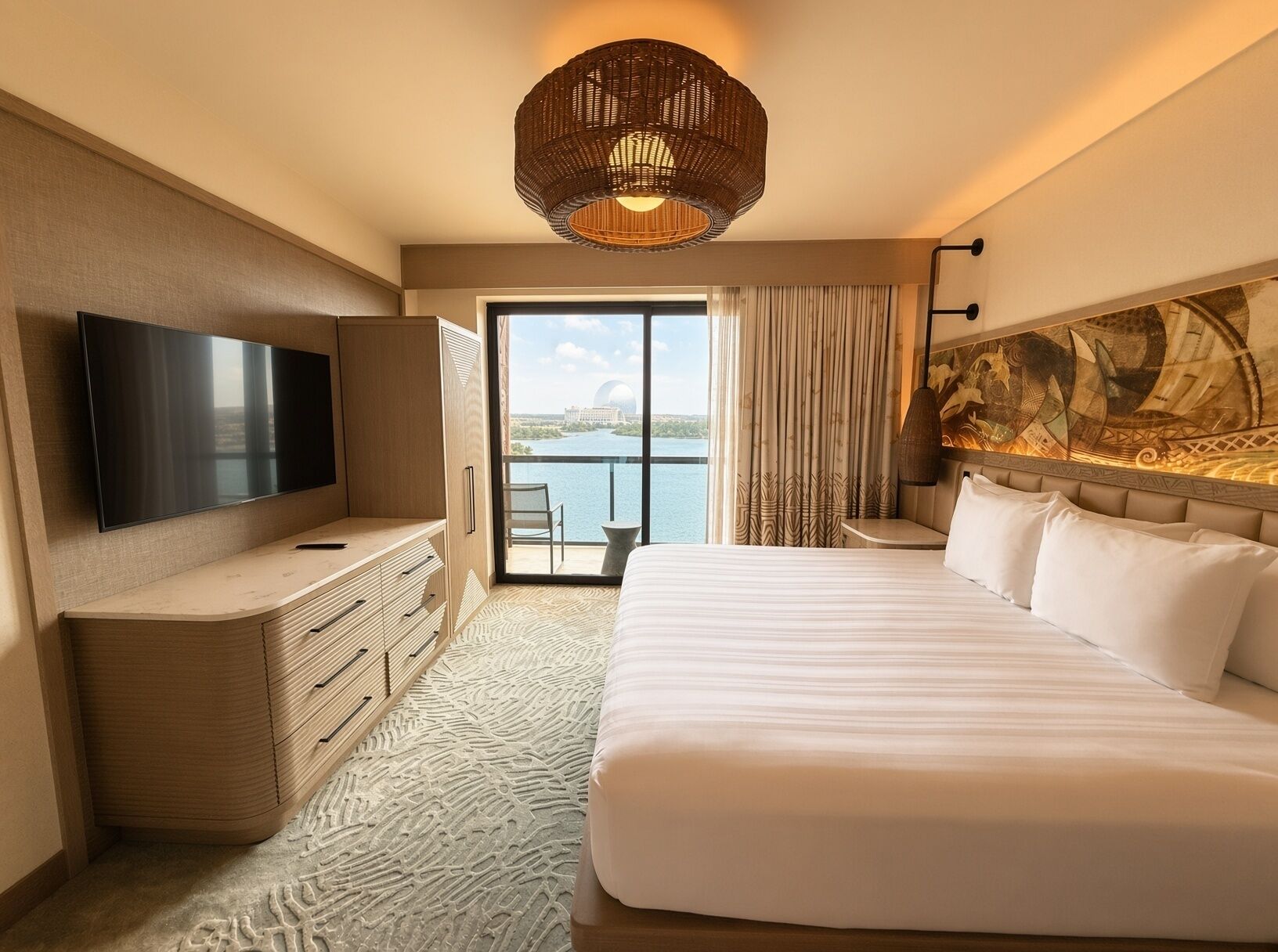 A hotel room with a large bed, a flat-screen TV, a desk, and a view of the water.