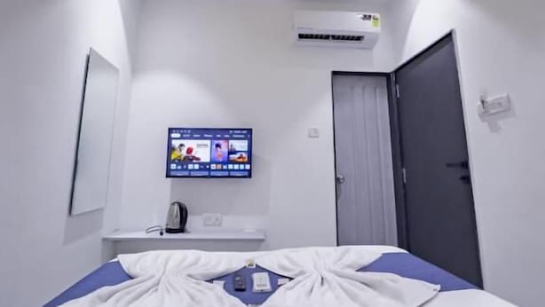 Habitación de hotel con cama, ventilador de techo, aire acondicionado, televisor en la pared y puerta.