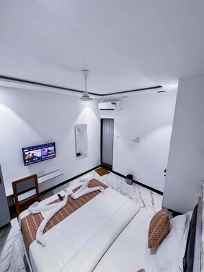 A hotel room with a bed, a television, a ceiling fan, and an air conditioning unit. - Hotel Flora Inn (Mumbai)