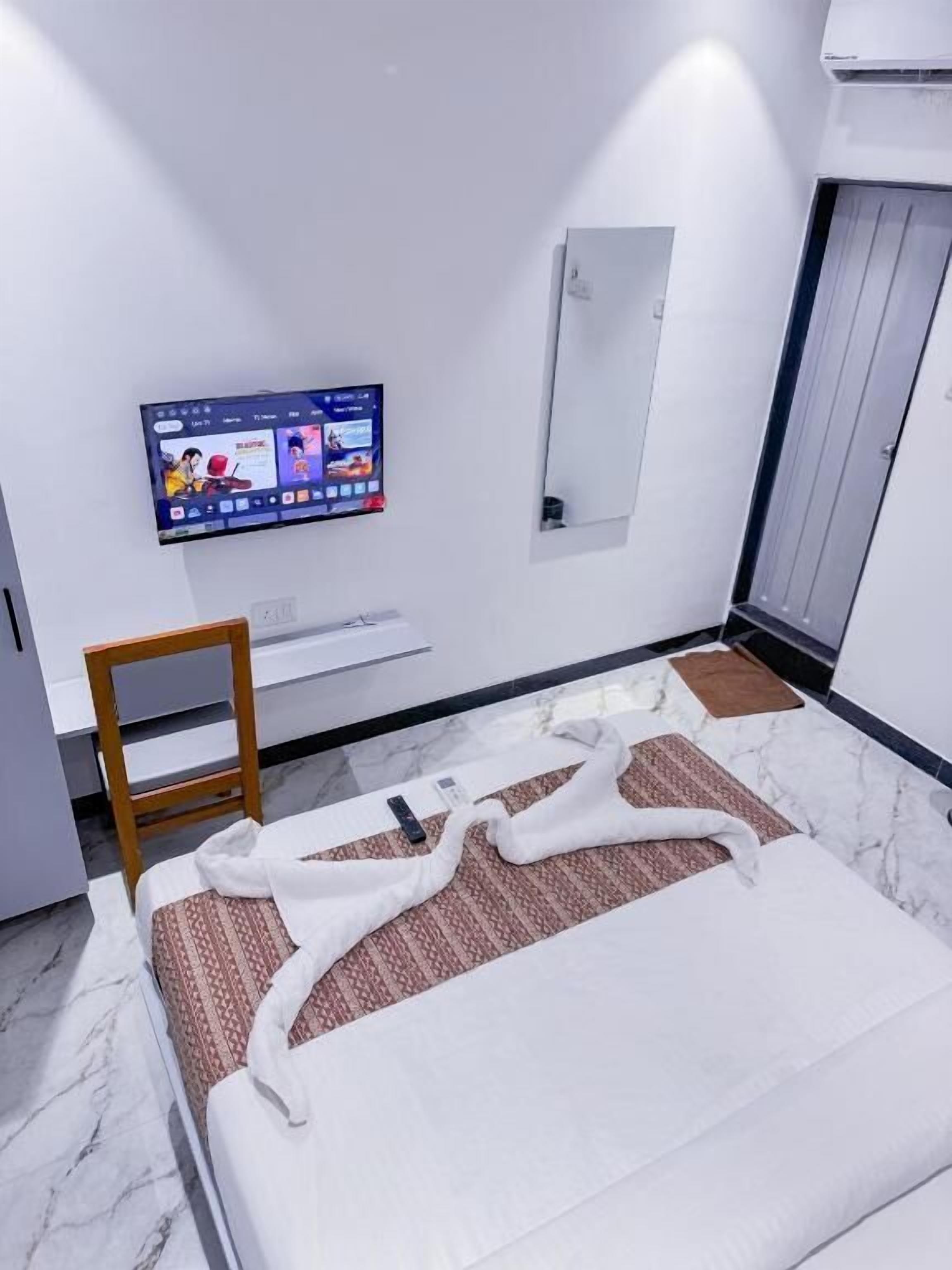 A modern hotel room with a bed, a television mounted on the wall, a mirror, and a door.