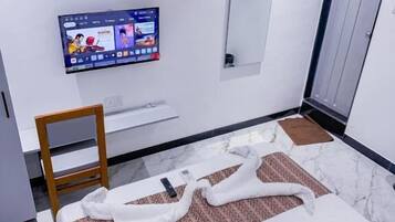 A modern hotel room with a bed, a television mounted on the wall, a mirror, and a door.