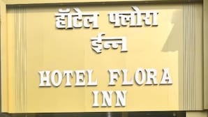 Entrada de un hotel con un cartel en hindi e inglés, un guardia de seguridad y un área alfombrada de color verde.