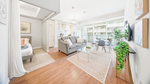 A modern living room with a grey sofa, a glass coffee table, and a dining area with chairs. - Founder's Club York - 3 Bedroom Condo  (Toronto)