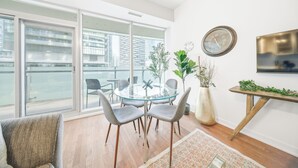 A modern living room with a glass table, grey chairs, a large window, and a view of the city. - Founder's Club York - 3 Bedroom Condo  (Toronto)