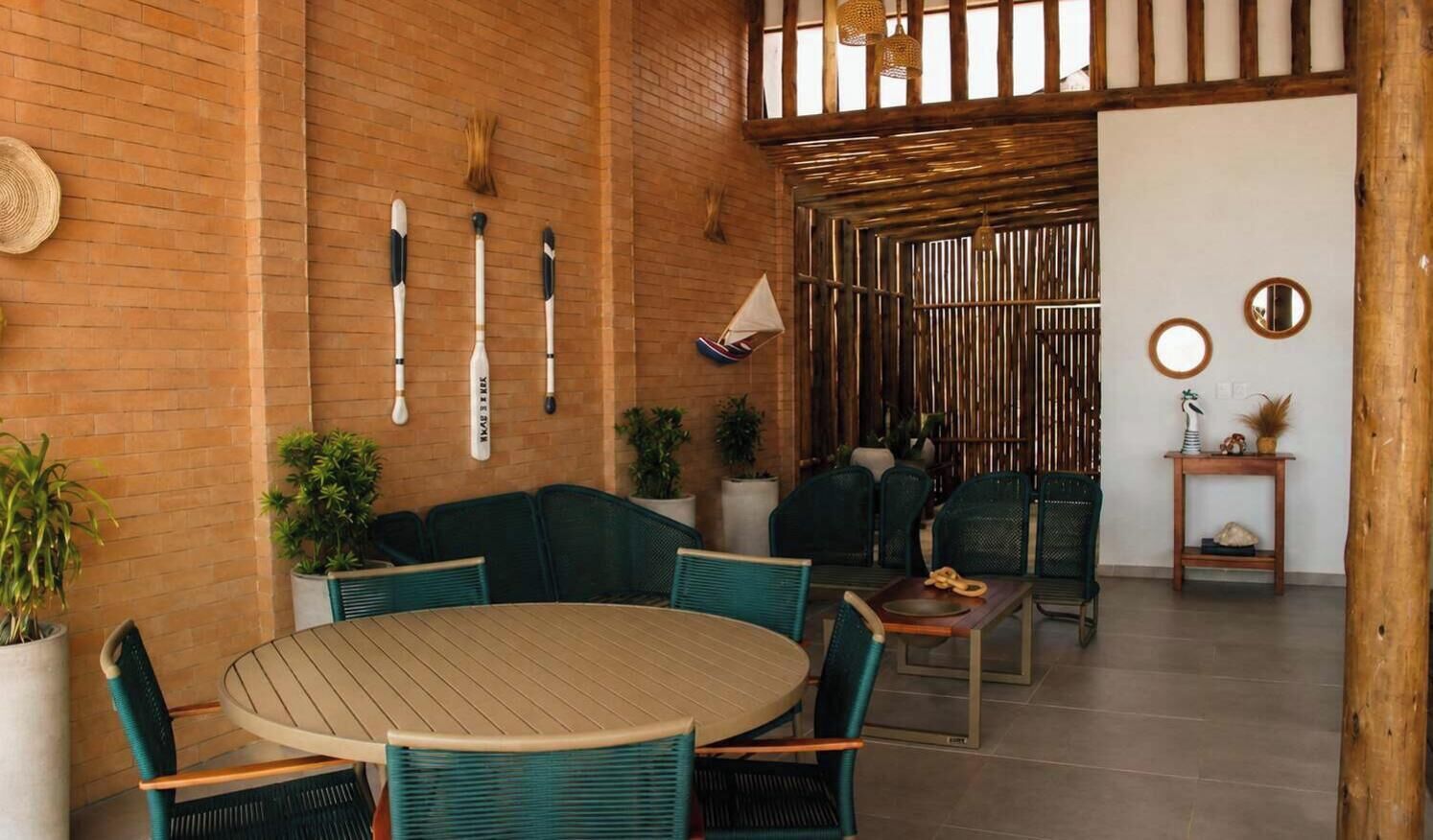 A cozy indoor seating area with a round table and chairs, a brick wall, and a wooden ceiling.
