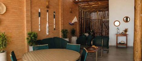 A cozy indoor seating area with a round table and chairs, a brick wall, and a wooden ceiling.
