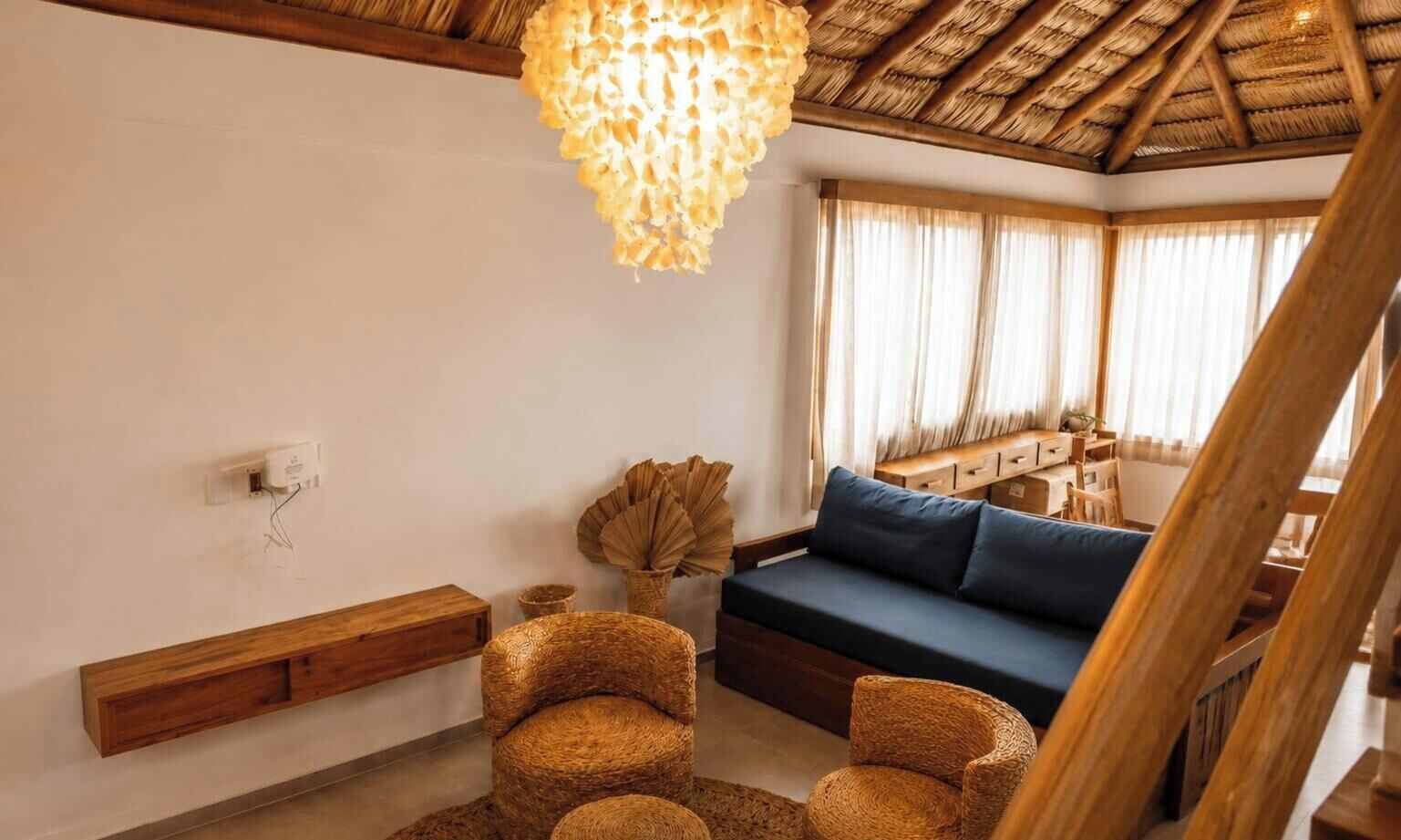 Uma sala de estar aconchegante com teto de madeira, um sofá azul, cadeiras de vime e um candeeiro pendente.