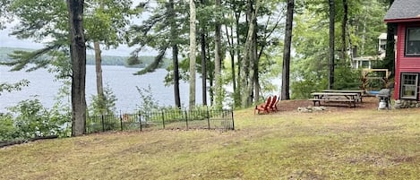 Una propiedad junto al lago con un edificio rojo, mesas de picnic y un área cercada.