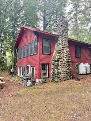 A two-story red house with a stone chimney, surrounded by trees. - WATERFRONT ON THOMAS POND (Casco)