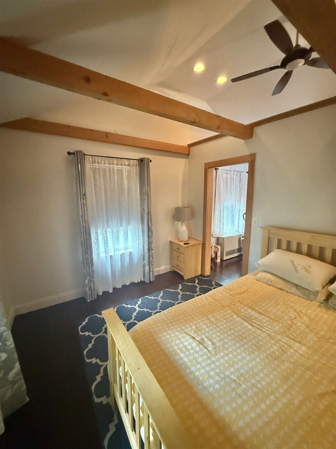 A bedroom with a bed, a nightstand, a lamp, a ceiling fan, and a window with curtains.