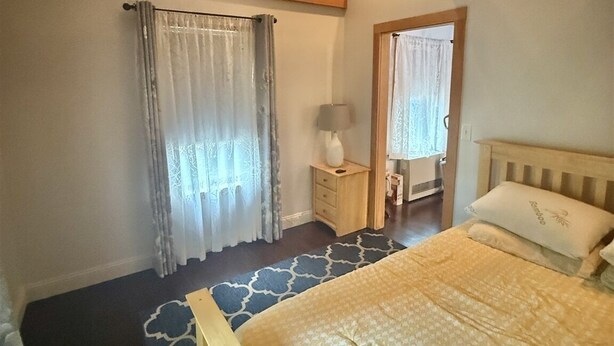 Ein Schlafzimmer mit einem Bett, einem Nachttisch, einer Lampe, einem Deckenventilator und einem Fenster mit Vorhängen.