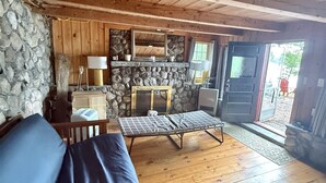 Ein gemütliches Blockhaus-Interieur mit Steinwand, Holzbalkendecke, einer Couch, einem Tisch und einer Bank.