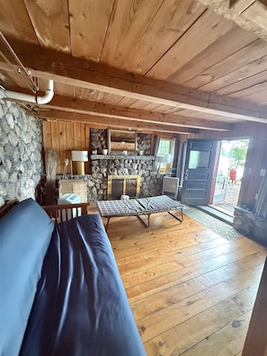 Ein gemütliches Blockhaus-Interieur mit Steinwand, Holzbalkendecke, einer Couch, einem Tisch und einer Bank.