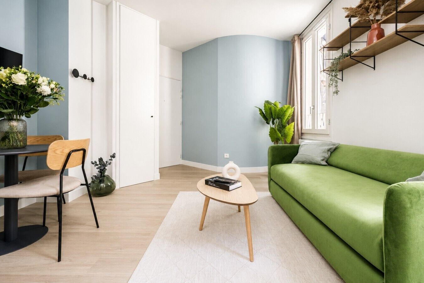 A modern living room with a green sofa, a dining table with chairs, and a coffee table with a book.