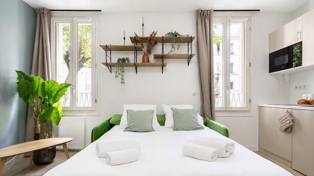 Et hotelværelse med seng, bænk, fjernsyn, mikroovn og en plante.