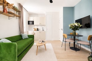 A modern living room with a green sofa, a coffee table, and a dining area with a table and chairs. - Lavie Maison: Elegant Studio near Montmartre (Paris)