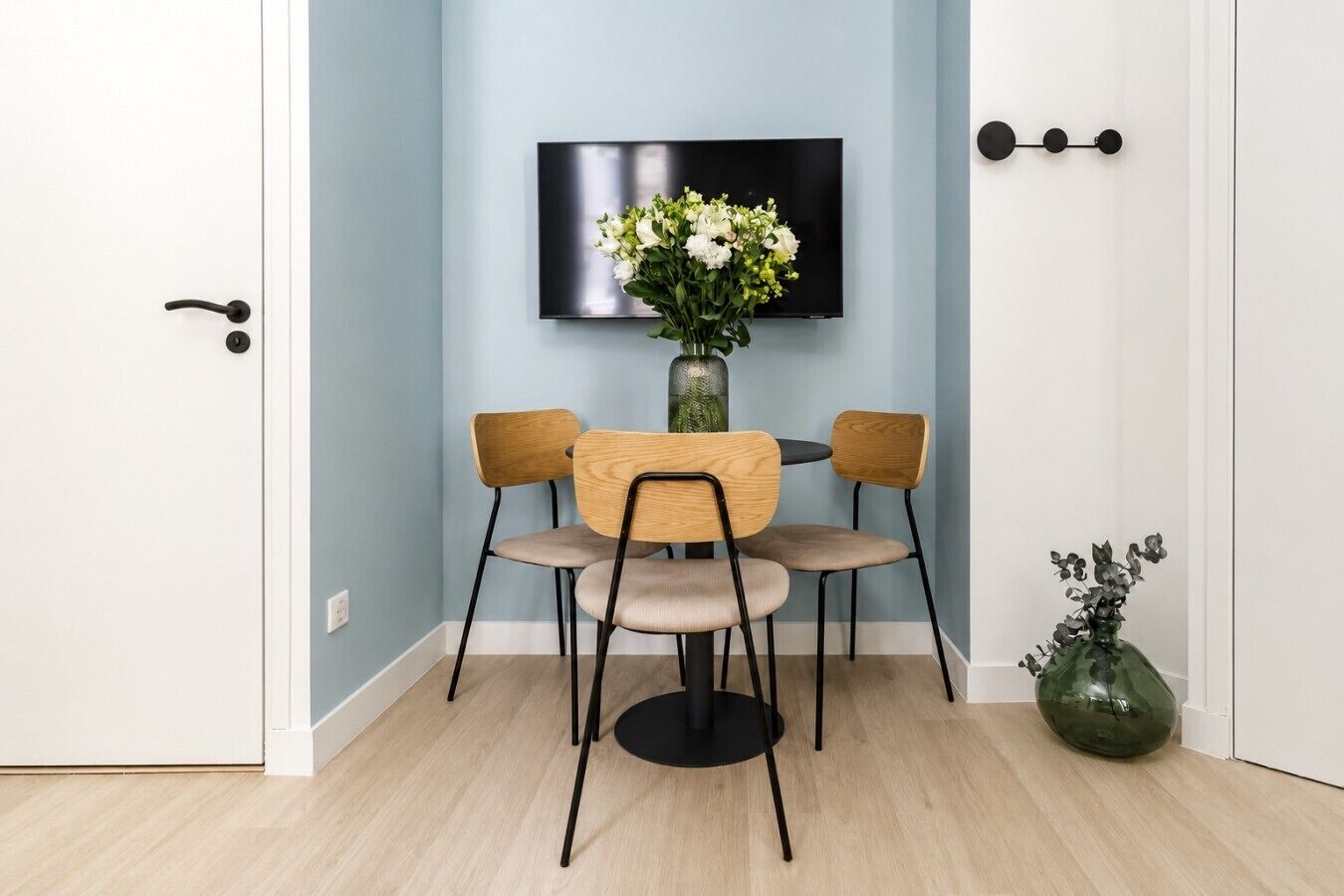 Ein Zimmer mit Esstisch und Stühlen, einem an der Wand befestigten Flachbildfernseher und einer Vase mit Blumen auf dem Boden.